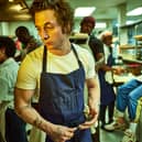 Jeremy Allen White as Carmen ‘Carmy’ Berzatto in The Bear, wearing a blue apron, holdin a spoon in a restaurant kitchen (Credit: Frank Ockenfels/FX )