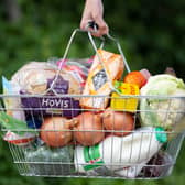 A woman holds a shopping basket of groceries.