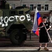 A man holds the Russian national flag in front of a Wagner group military vehicle with the sign read as "Rostov" in Rostov-on-Don late on June 24, 2023. Rebel mercenary leader Yevgeny Prigozhin who sent his fighters to topple the military leaders in Moscow will leave for Belarus and a criminal case against him will be dropped as part of a deal to avoid "bloodshed," the Kremlin said on June 24. (Photo by STRINGER / AFP) (Photo by STRINGER/AFP via Getty Images)