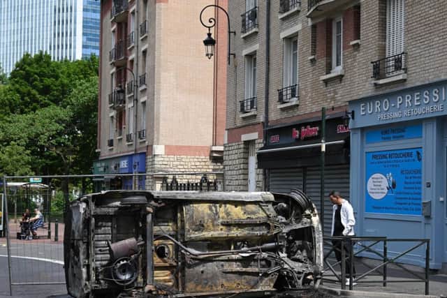 A pedestrian looks at an overturned burnt car in the street in Puteaux, west of Paris on June 30, 2023. (BERTRAND GUAYAFP via Getty Images)