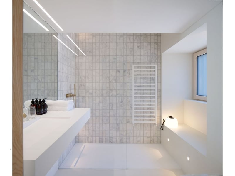 The immaculate bathroom has white marble tiles, a rain shower, underfloor heating, and fluffy towels. 