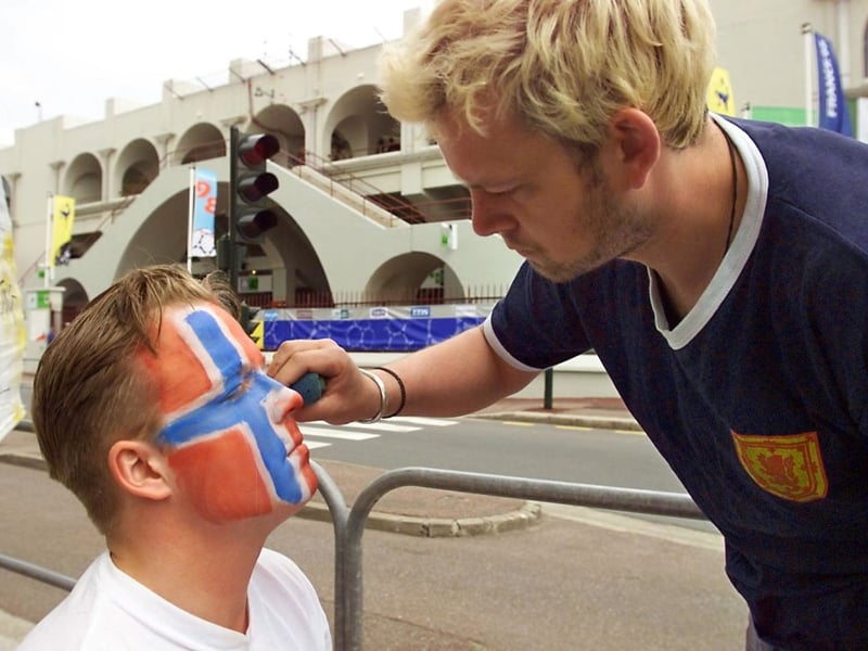 One Scotland fan helps a Norway supporter paint his face in the colour of the Norwegian flag.