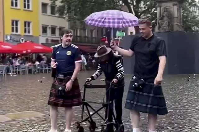 Two Tartan Army foot-soldiers shelter an elderly German in a Cologne downpour. A special photo.