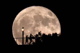 People walk in front of a rising supermoon at Griffith Observatory in Los Angeles