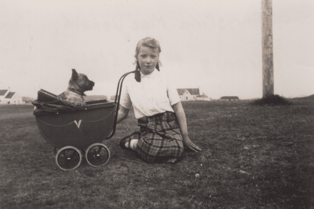 Christina MacDonald, the daughter of an island policeman, playing with her dog in a toy pram outside Cornaig police station around the 1940s.