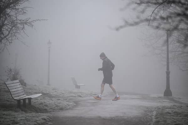 A jogger makes their way through fog on a frosty morning.