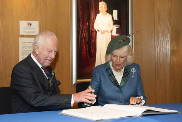 King Charles III and Queen Consort Camilla sign the Scottish Parliament visitors’ book, with a portrait of the late Queen Elizabeth II in the background.