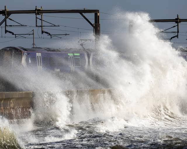 A train passes as waves crash against the sea defences as storm Ashley arrives in Saltcoats