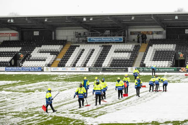 Stewards help clear snow off the pitch ahead of St Mirren and Aberdeen at the SMiSA Stadium.