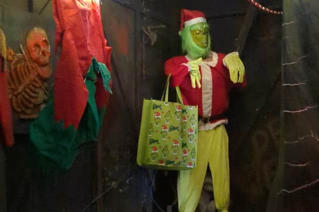 A Grinch decoration with a Grinch tote bag stood at the end of the attraction beside Halloween decorations on the wall.