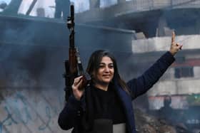 An armed woman flashes the V for victory sign as Syrian Kurds celebrate the fall of capital Damascus to anti-government fighters, in the city of Qamishli