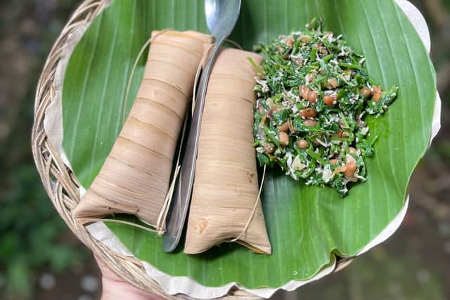 A meal of steamed uraban vegetables in a peanut and coconut mix with packets of rice made by villagers in Sibetan