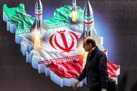 A man walks past a pro-regime banner in central Tehran depicting missiles launching from a map of Iran (Picture: Atta Kenare)