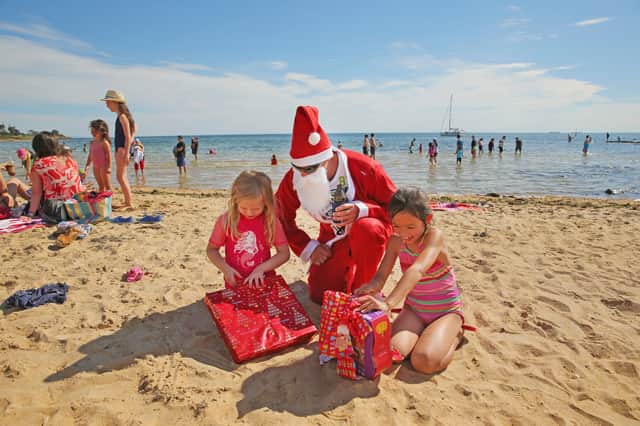 Santa Claus watches as two children open their presents on Brighton Beach in Melbourne, Australia (Picture:  Scott Barbour)