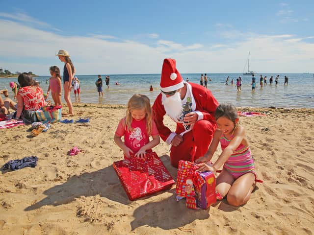 Santa Claus watches as two children open their presents on Brighton Beach in Melbourne, Australia (Picture:  Scott Barbour)