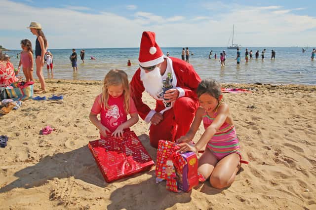 Santa Claus watches as two children open their presents on Brighton Beach in Melbourne, Australia (Picture: Scott Barbour)