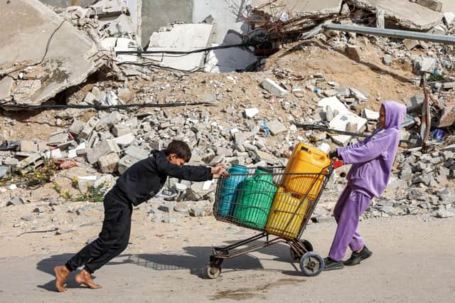 A girl and a boy move a shopping trolley loaded with water containers past a mound of rubble in Gaza City on December 11 (Picture: Omar al-Qattaa)