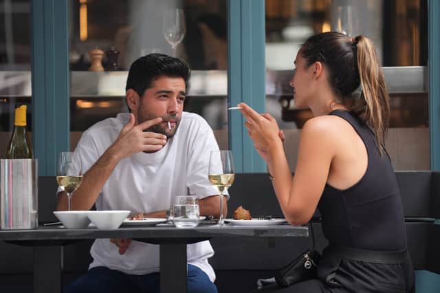 People smoking cigarettes while sitting outdoors at a restaurant, in Soho, London
