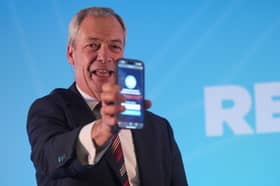 Reform UK leader Nigel Farage holding a phone displaying the number of Reform UK party members whilst speaking during the Reform UK East of England conference at Chelmsford City Racecourse
