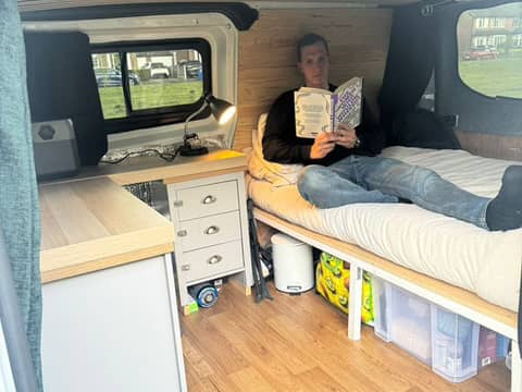 Dom Wright reads inside the back of his converted Ford Transit van