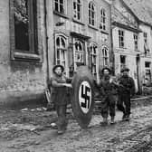 The road to German surrender: Privates H McIvor, W Harton and D Mill from the 10th Highland Light Infantry,15th Scottish Infantry Division, roll a wooden Swastika emblem through Kranenberg during Operation Veritable  on February 10, 1945 at Kranenberg. Scots had a heavy presence in Germany during this period, which led to Operation Plunder and the crossing of the Rhine, the last big set piece ahead of the German surrender.
  British Official Photo B. 14427 (WT). (Photo by Sergeant Norman Midgley/No.5 Army Film & Photographic Unit/BIPPA/Keystone/Hulton Archive/Getty Images).