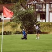 A golfer chips on to a green, with Spey Valley apartments in the background