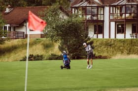 A golfer chips on to a green, with Spey Valley apartments in the background