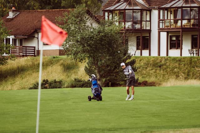 A golfer chips on to a green, with Spey Valley apartments in the background
