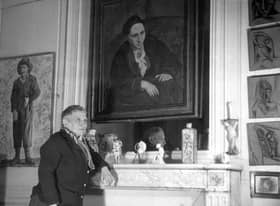 At her apartment in Paris, Gertrude Stein (1874-1946) poses in front of the portrait of her painted by Pablo Picasso in 1906 