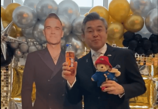 Hiroshi Suzuki trying Irn Bru next to a cardboard cutout of Robbie Williams, who is playing Murrayfield this weekend.