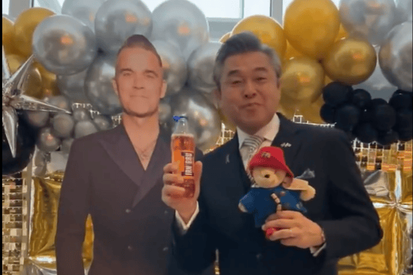 Hiroshi Suzuki trying Irn Bru next to a cardboard cutout of Robbie Williams, who is playing Murrayfield this weekend.