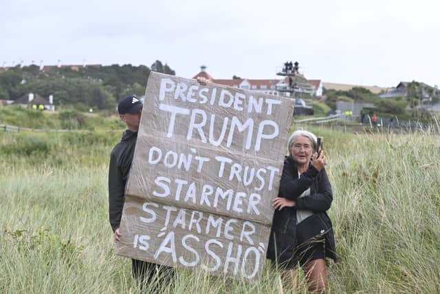 Supporters of the US president holding a sign as their friend shouts 'we love you Trump' from the edge of the Turnberry golf course
