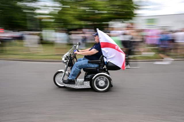 A demonstrator rides an electric scooter flying a St George's flag during an anti-immigration protest outside the Sheraton Four Points hotel in south London (Picture: Ben Stansall)