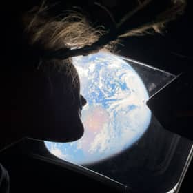 Astronaut Christina Koch peers out of one of Artemis II's windows, looking back at Earth as the crew travels towards the Moon