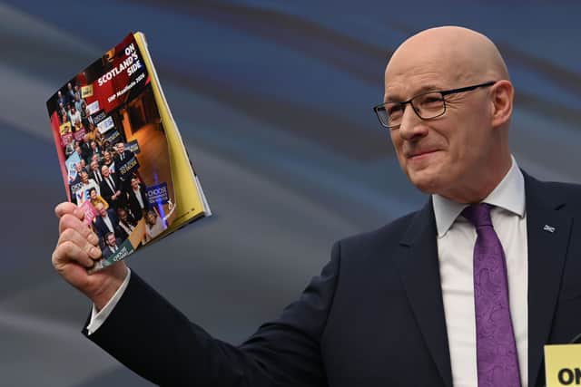 John Swinney smiles while holding up a copy of the SNP manifesto