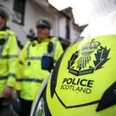 Police Scotland officers in uniform, walking past a police motorbike
