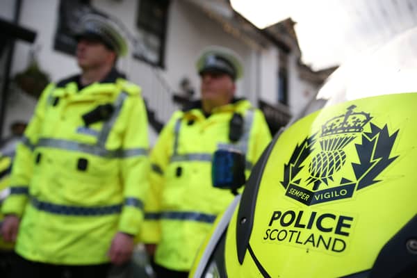 Police Scotland officers in uniform, walking past a police motorbike