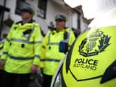 Police Scotland officers in uniform, walking past a police motorbike