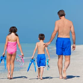 A happy family of mother, father and child, a daughter, walking in swimming costumes on a sunny beach