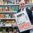 John Swinney in a shop, holding up a sign advertising the SNP's food price cap proposal