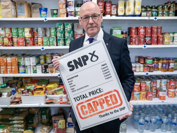 John Swinney in a shop, holding up a sign advertising the SNP's food price cap proposal