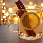 A festive hot toddy served in a clear glass mug, garnished with a lemon slice and a cinnamon stick, with a background of glowing Christmas lights reflecting off a frosted window.