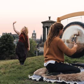 Madeleine Schmoll of The Scotch Malt Whisky Society raising a toast to the start of whisky season on Calton Hill, Edinburgh, with Jo McCoy of Blissness, a gong sound bath practitioner