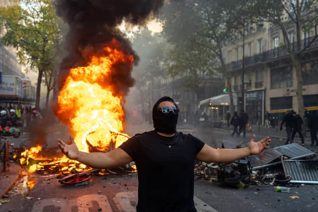 A protester poses in front of a fire as his friend takes a photograph during demonstrations in Paris