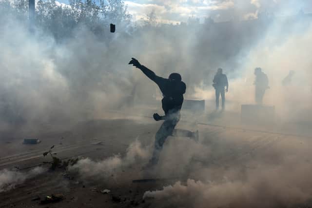A protester throws a rock in thick tear gas during demonstrations in Paris