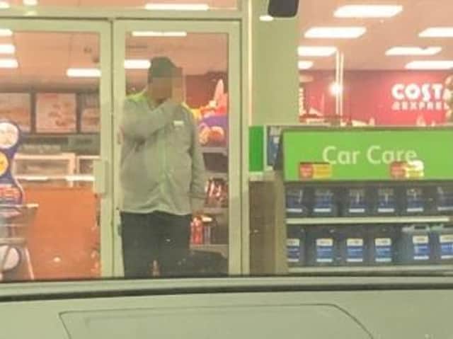 The worker appears to be smoking a cigarette outside the petrol station shop.