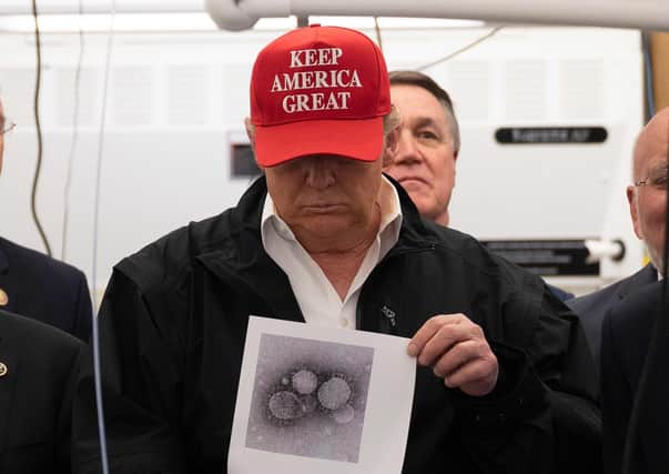 Donald Trump, wearing a ‘keep America great’ cap, holds a picture of the coronavirus (Picture: Jim Watson/AFP via Getty Images)