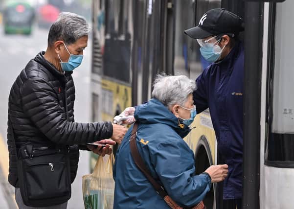 A bus employee wearing goggles and a face mask checks the temperature of passengers before they board a bus in Wuhan, where the lockdown has been lifted by the Chinese authorities (Picture: Hector Retamal/AFP via Getty Images)