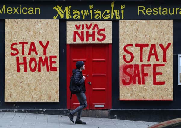 A person passes a boarded up restaurant in Edinburgh which has been painted with an NHS supporting message. Picture: PA