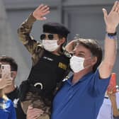 Brazil's President Jair Bolsonaro, wearing a mask, carries a child dressed in a military police uniform during a protest against the National Congress's restrictions and in support of his open-the-economy drive (Picture: Andre Borges/AP)